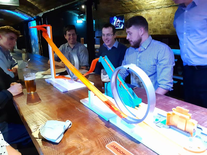 Group of people in a pub with a toy track on the table.